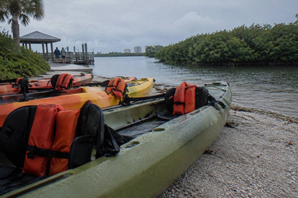 Tandem kayaks lined up on a sandy launch beside calm mangrove water