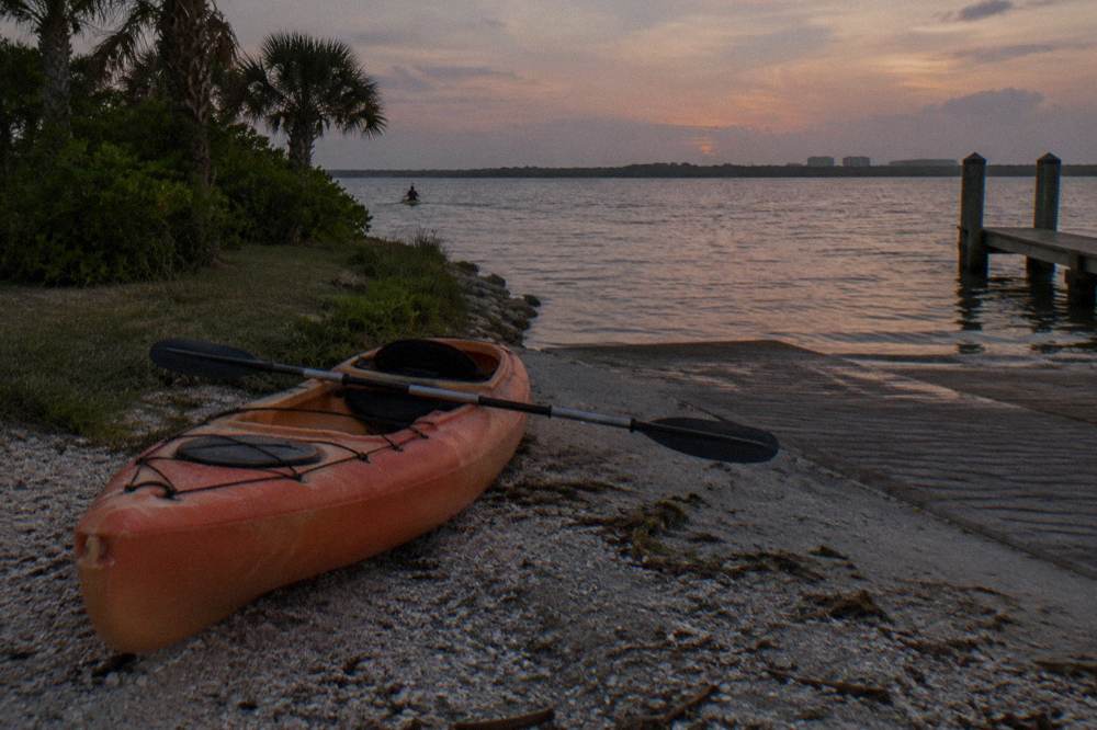 A kayak resting on a sandy launch beside calm evening lagoon water