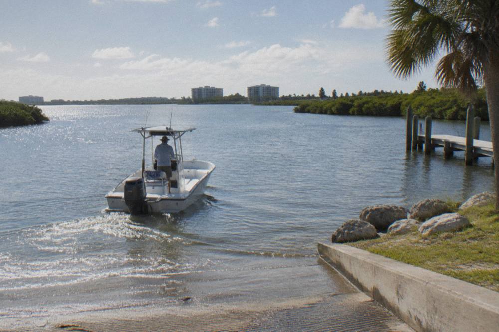 A powerboat moving slowly through a shallow lagoon channel marked by speed zone signs