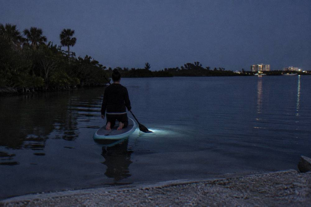 Paddleboarder kneeling on dark water with a soft glow ring spreading from the board