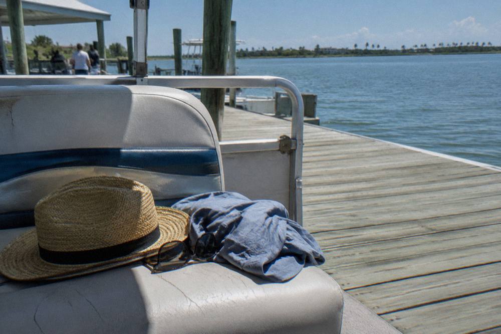 Sun hat, sunglasses and quick-dry shirt resting on a boat seat beside a lagoon