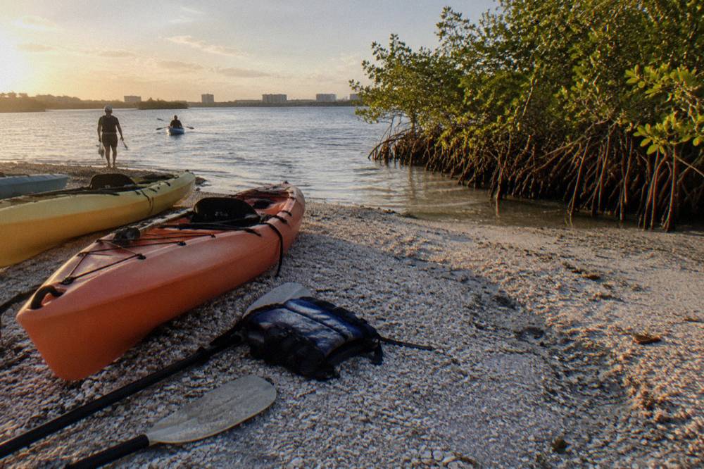 Kayaks beached at a lagoon launch point with paddle gear laid out on the sand