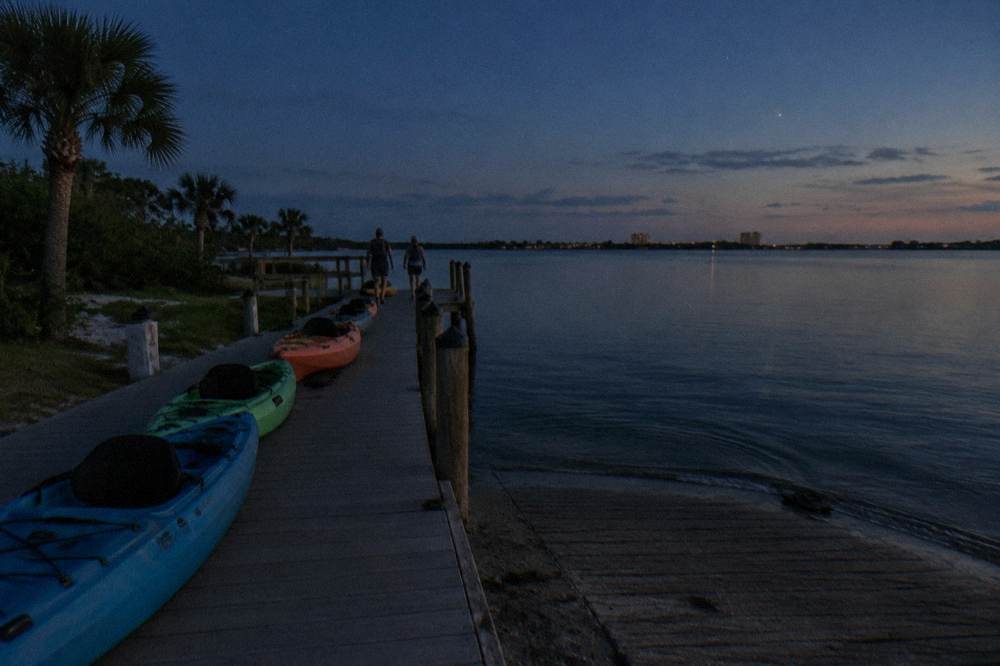 Calm dark lagoon water at dusk with kayaks lined up on a launch ramp