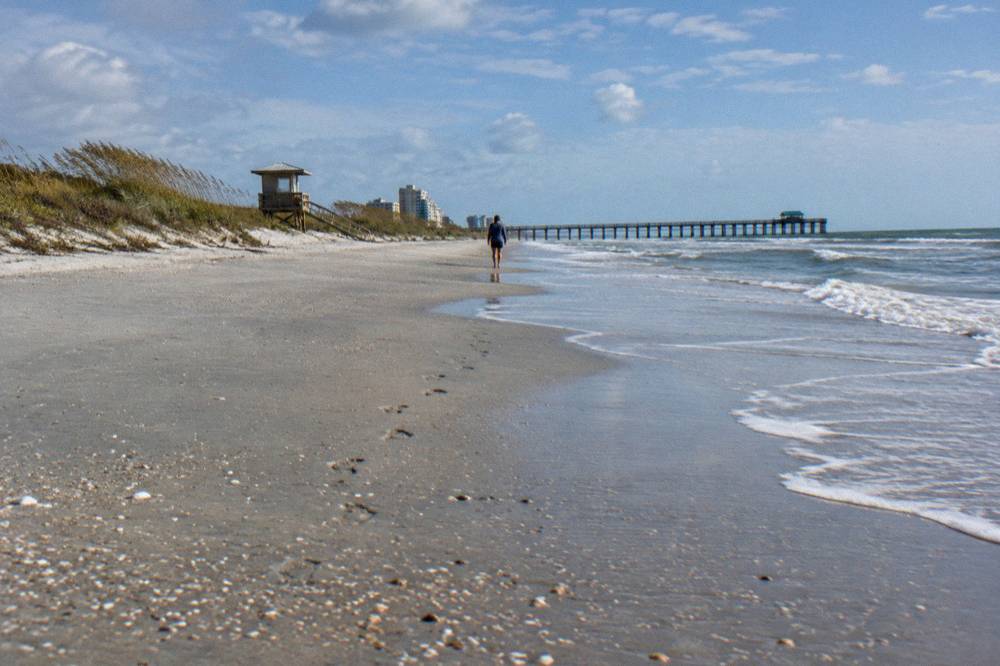A wide sandy beach with gentle surf and a low dune line under a clear sky