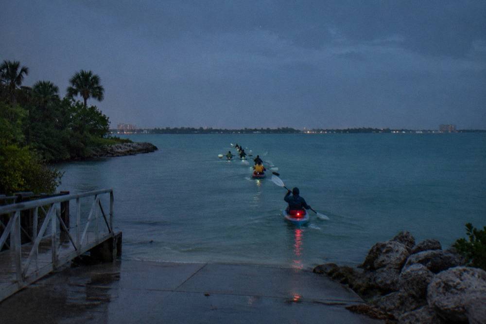 A line of kayaks gliding across glowing turquoise water beneath a starry sky