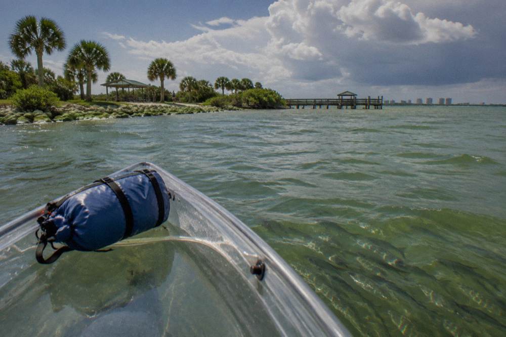 A transparent hull kayak on green lagoon water with fish visible beneath the surface