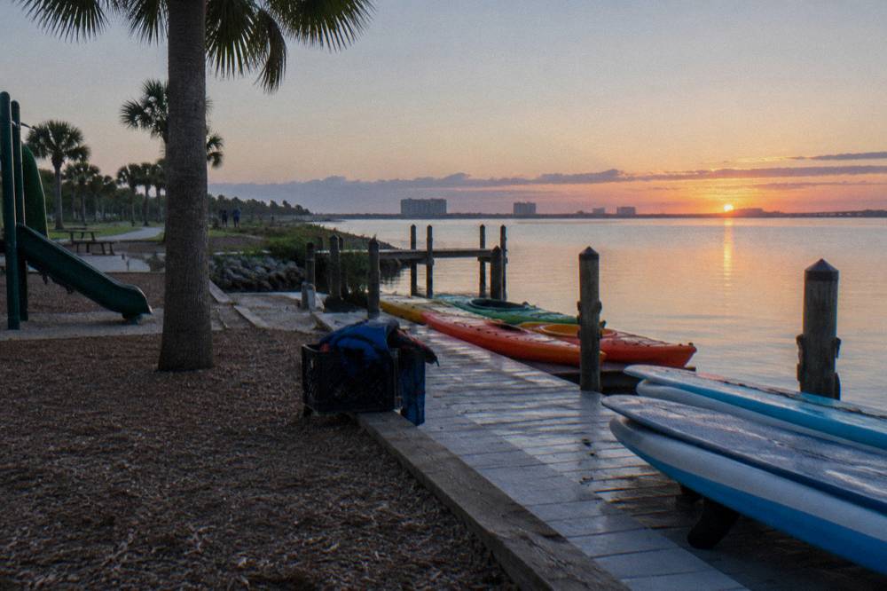 Kayaks and paddleboards lined up on a dock beside calm Banana River water