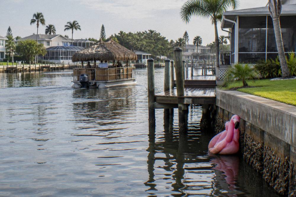 A tiki-style boat with thatched canopy drifting past waterfront homes
