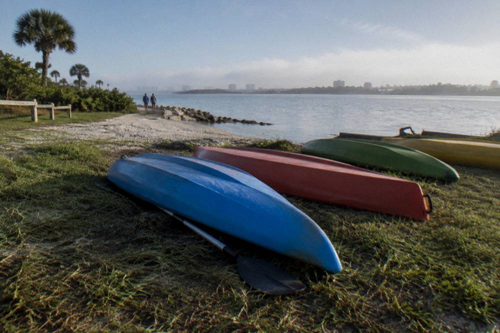 Kayaks lined up on a grassy bank beside a sheltered lagoon launch area