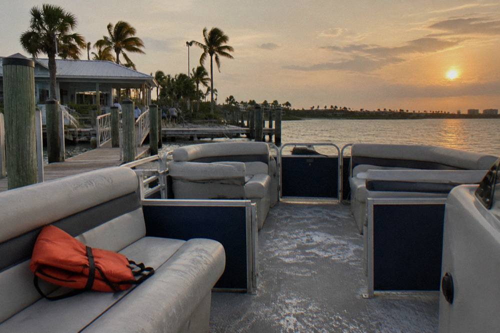A covered pontoon boat with rows of seats moving across a calm lagoon