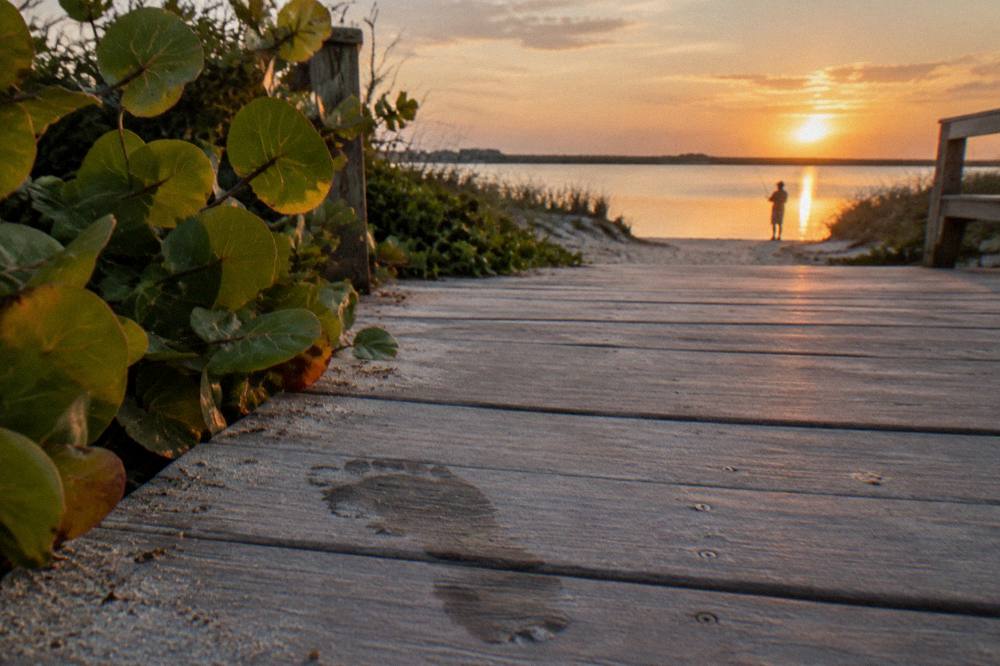 A wooden boardwalk and calm lagoon shoreline at a Cocoa Beach park at golden hour