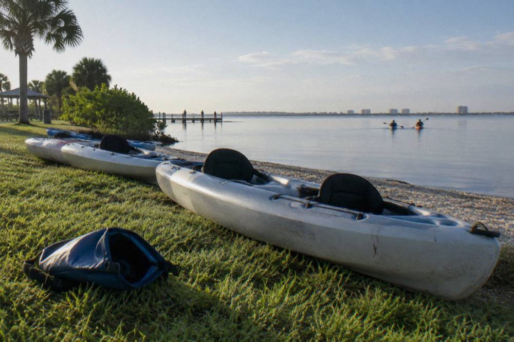 Tandem kayaks lined up on a grassy launch bank beside calm lagoon water