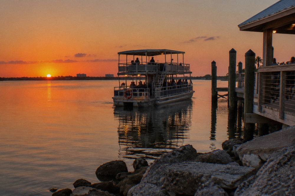A pontoon boat cruising calm lagoon water under a deep orange sunset sky