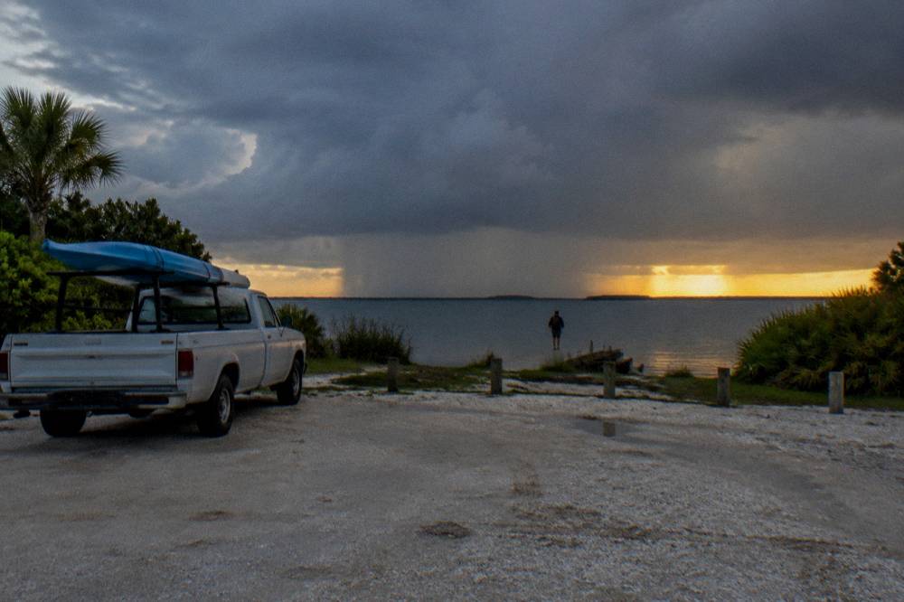 Dark storm clouds building over a calm lagoon with sunlight breaking at the horizon