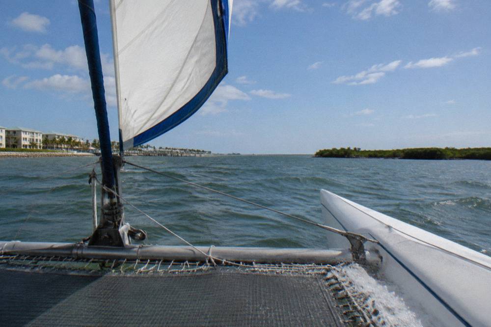 A small sailing catamaran under way on open lagoon water with clear sky