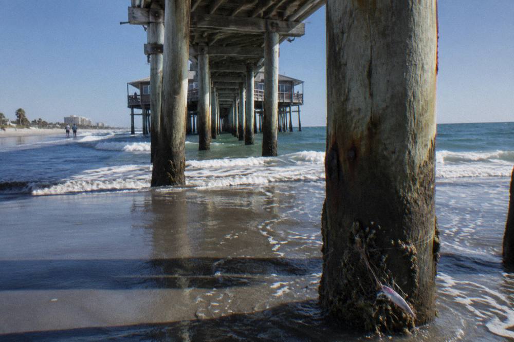 Long wooden fishing pier extending over dark green Atlantic water under a clear sky