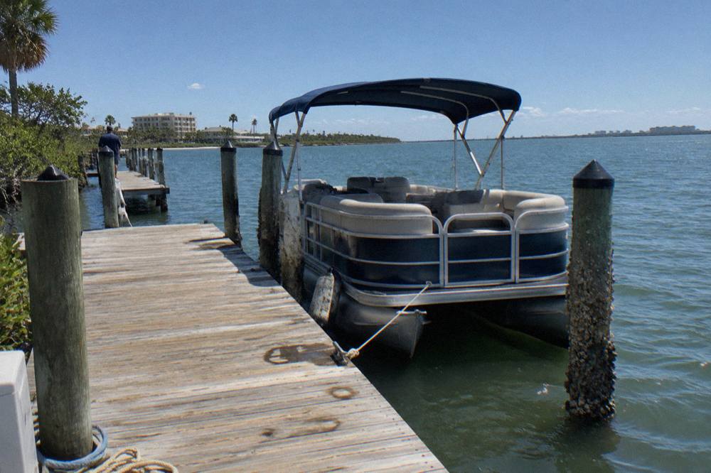 Covered pontoon boat tied at a wooden dock on a lagoon in Cocoa Beach